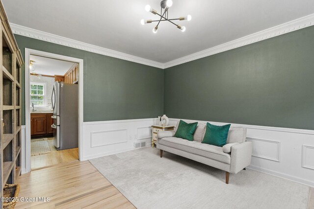 55 Journey Ln, Bethlehem, NY 12077 - living area featuring a chandelier, wainscoting, light wood-style flooring, crown molding, and a decorative wall
