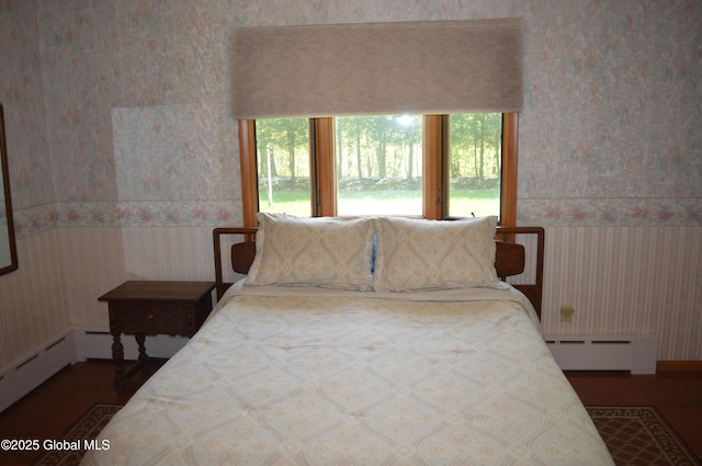 bedroom featuring wallpapered walls, a baseboard radiator, wood finished floors, and a wainscoted wall