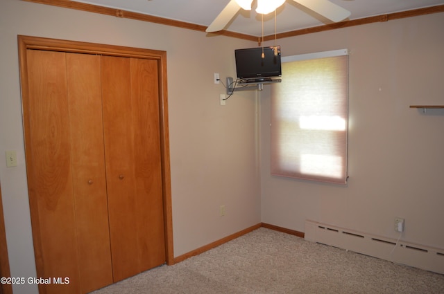 unfurnished bedroom featuring baseboard heating, carpet floors, a closet, ornamental molding, and a ceiling fan