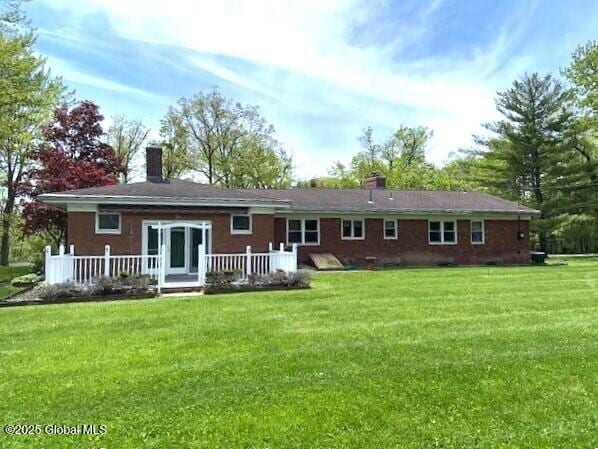 rear view of house featuring a chimney, a lawn, and a wooden deck