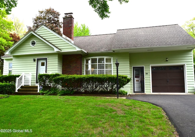ranch-style home featuring driveway, roof with shingles, a chimney, a front yard, and an attached garage