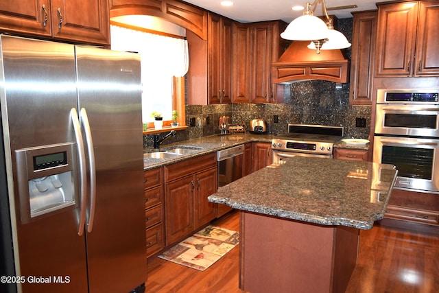 kitchen with appliances with stainless steel finishes, a sink, a kitchen island, dark wood finished floors, and dark stone countertops