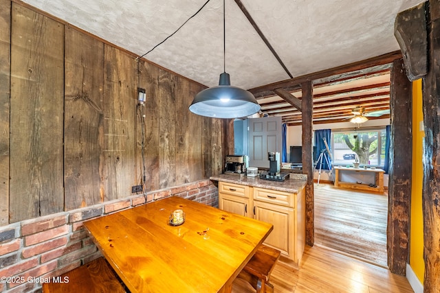 dining room featuring wood walls, light wood finished floors, and beamed ceiling