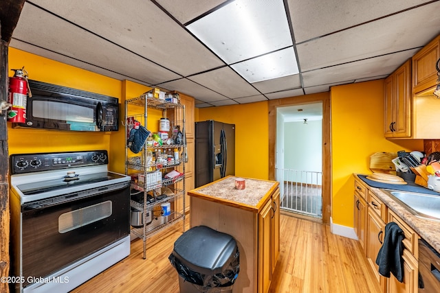 kitchen featuring black appliances, light wood-style flooring, light countertops, and a drop ceiling