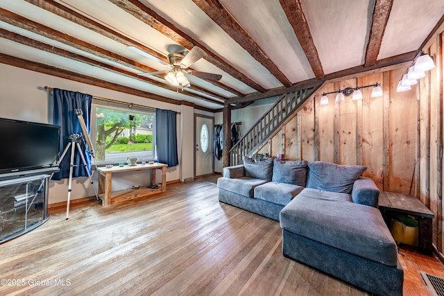 living room featuring stairs, a ceiling fan, beamed ceiling, hardwood / wood-style floors, and baseboards