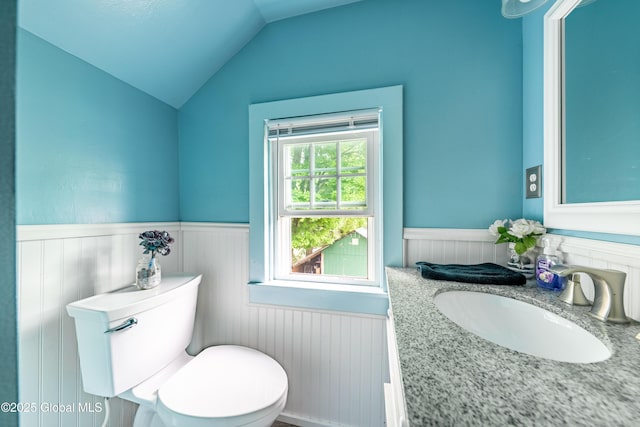 bathroom featuring a wainscoted wall, lofted ceiling, toilet, and vanity
