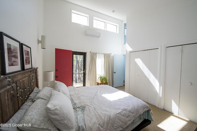 bedroom with a wall mounted air conditioner, a high ceiling, two closets, and light colored carpet