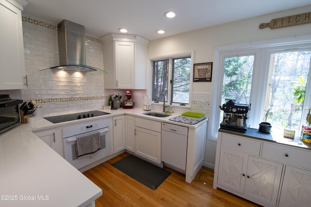 kitchen with white appliances, wall chimney exhaust hood, a sink, backsplash, and light wood-style floors