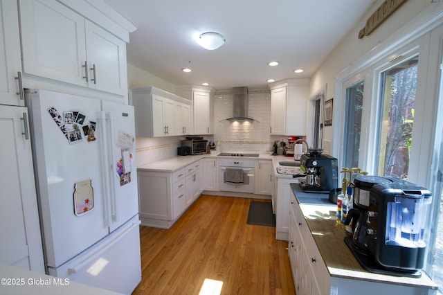 kitchen with white appliances, wall chimney exhaust hood, backsplash, a sink, and light wood-style flooring