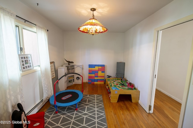 rec room with baseboard heating, wood finished floors, and baseboards