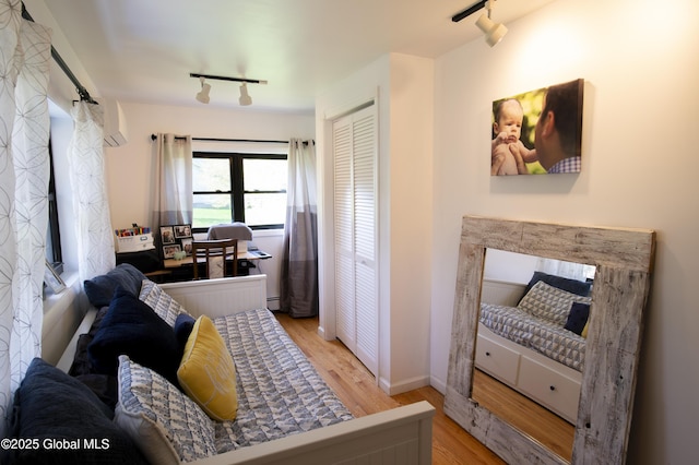 bedroom featuring track lighting, wood finished floors, a baseboard radiator, and baseboards