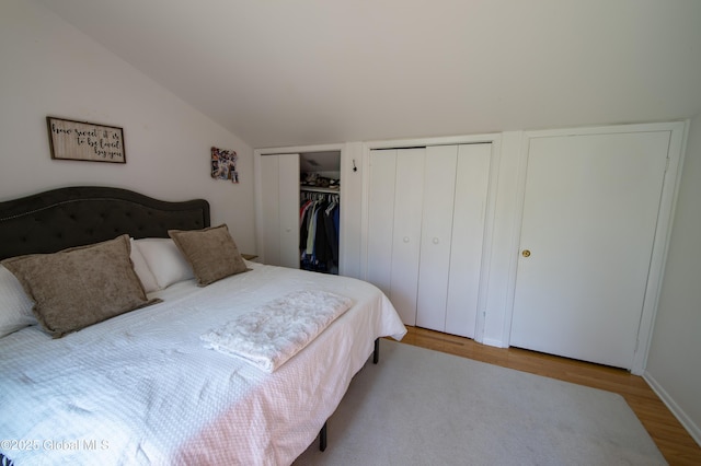 bedroom with two closets, wood finished floors, and vaulted ceiling