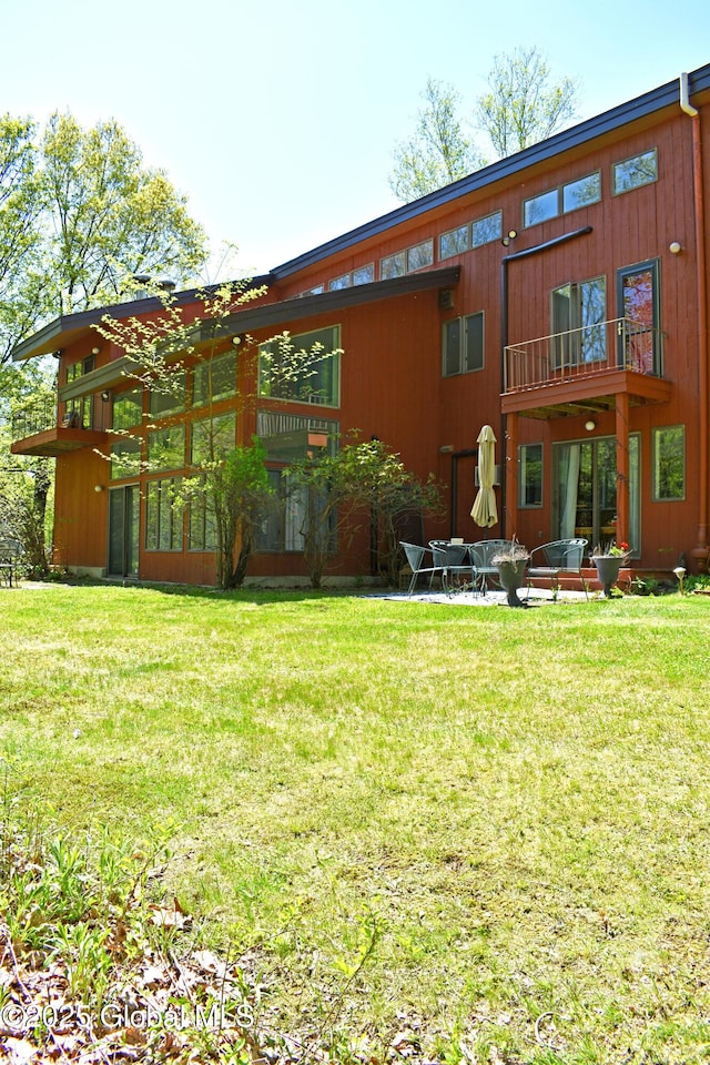 back of house featuring a lawn and a balcony