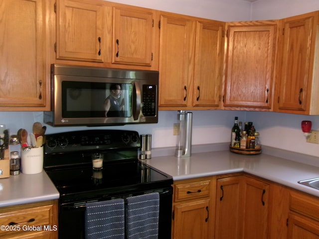 kitchen featuring stainless steel microwave, black electric range oven, light countertops, and brown cabinetry