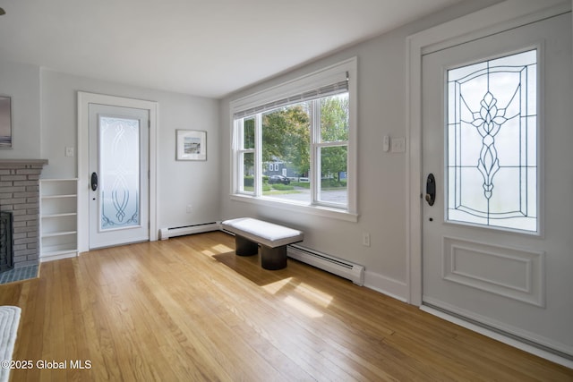 foyer entrance featuring a baseboard heating unit, a brick fireplace, and light wood-style flooring
