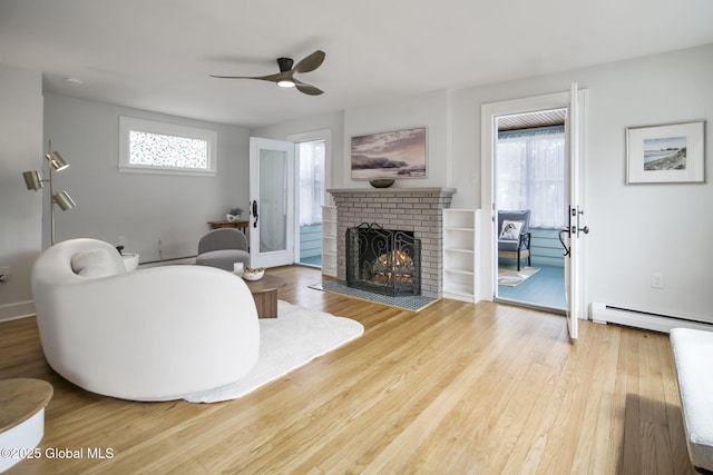 living room featuring a ceiling fan, a fireplace, wood finished floors, and baseboard heating