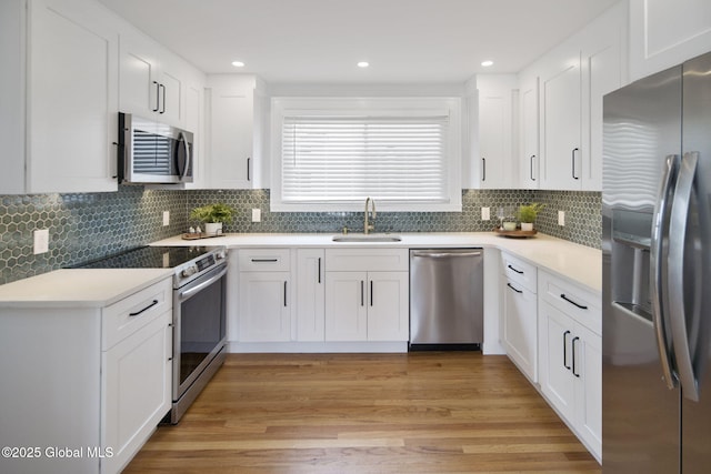 kitchen with stainless steel appliances, a sink, white cabinetry, light wood-type flooring, and decorative backsplash