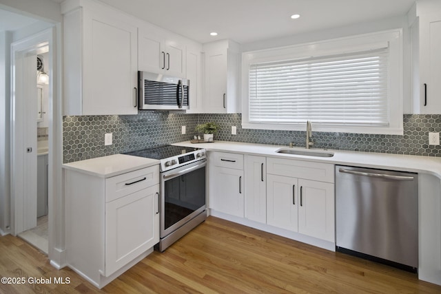 kitchen featuring appliances with stainless steel finishes, a sink, white cabinetry, light wood-style floors, and light countertops