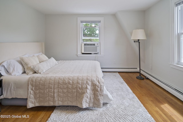 bedroom featuring a baseboard heating unit, wood finished floors, and cooling unit