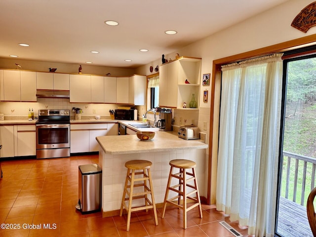 kitchen with stainless steel electric range oven, a sink, under cabinet range hood, light countertops, and a peninsula