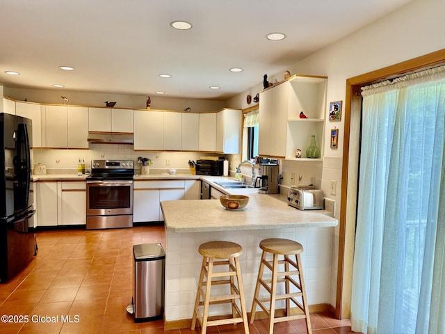 kitchen with stainless steel appliances, under cabinet range hood, a peninsula, a sink, and decorative backsplash