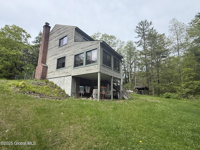 rear view of property featuring a chimney, a lawn, and stairs