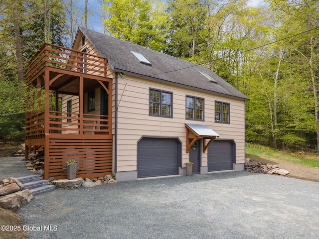 view of front of home with a garage, driveway, roof with shingles, and a wooden deck