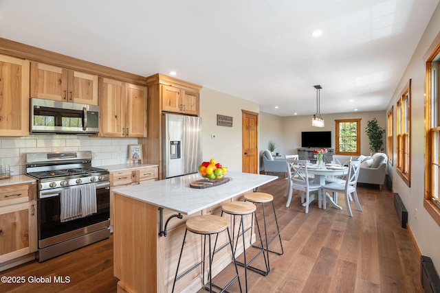 kitchen featuring appliances with stainless steel finishes, open floor plan, dark wood finished floors, decorative backsplash, and a kitchen bar