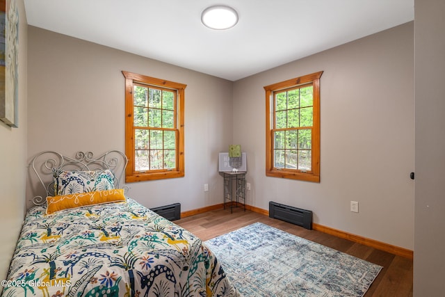 bedroom with multiple windows, wood finished floors, and baseboards