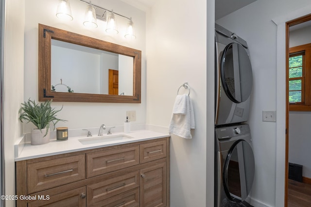bathroom with stacked washing machine and dryer, vanity, baseboards, and wood finished floors