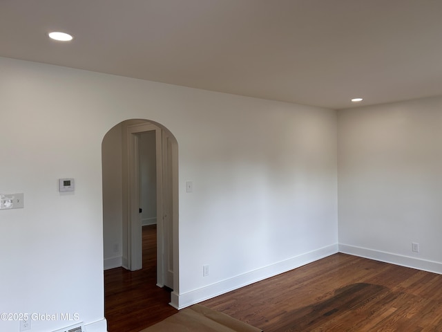 unfurnished room with arched walkways, recessed lighting, dark wood finished floors, and baseboards