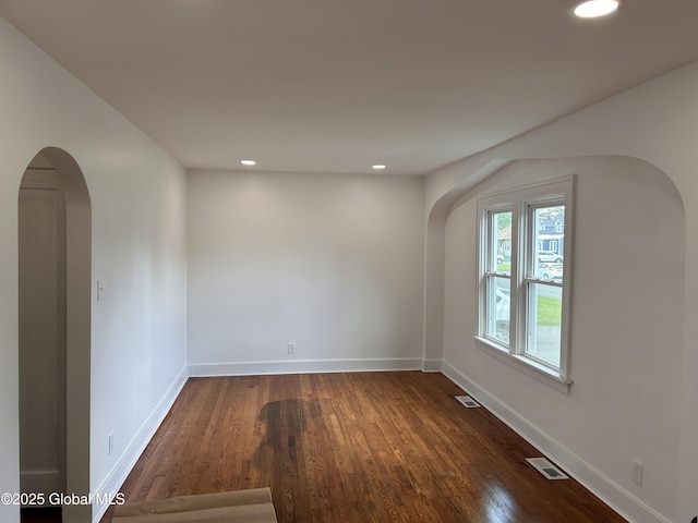 spare room with arched walkways, dark wood-type flooring, recessed lighting, and baseboards