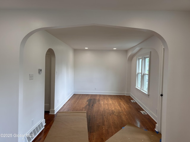 empty room featuring arched walkways, wood finished floors, and baseboards