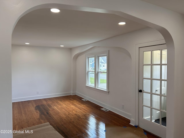 empty room featuring arched walkways, wood finished floors, baseboards, and recessed lighting