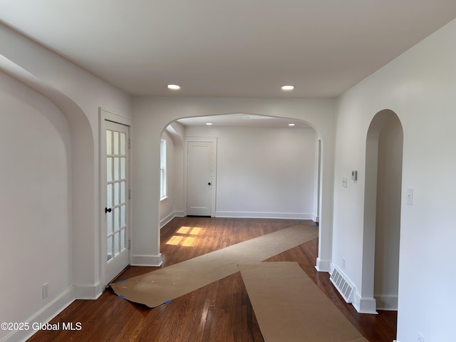 hallway with arched walkways, recessed lighting, wood finished floors, and baseboards