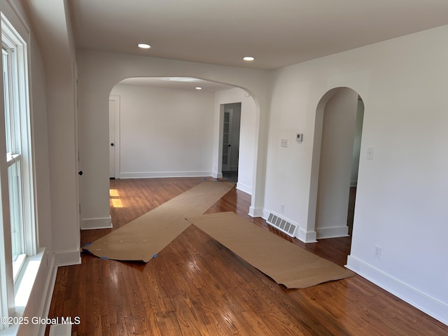 unfurnished room with arched walkways, wood finished floors, recessed lighting, and baseboards