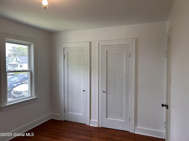 unfurnished bedroom featuring dark wood-style flooring, baseboards, and multiple closets