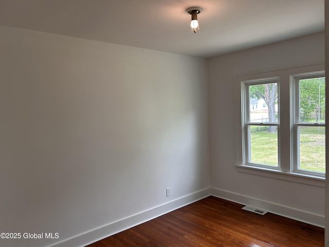 empty room featuring plenty of natural light, baseboards, and dark wood-type flooring