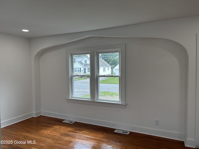 unfurnished room featuring arched walkways, baseboards, wood finished floors, and recessed lighting