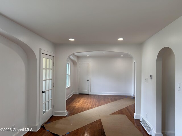 hallway with arched walkways, dark wood-style flooring, recessed lighting, and baseboards