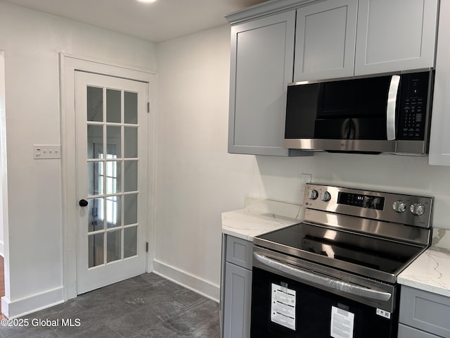 kitchen featuring stainless steel appliances, gray cabinetry, baseboards, and light stone counters
