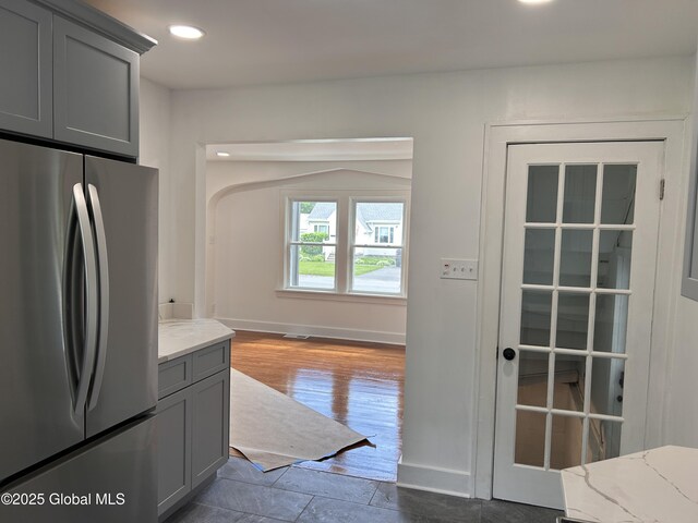 kitchen featuring freestanding refrigerator, gray cabinetry, light stone countertops, recessed lighting, and baseboards