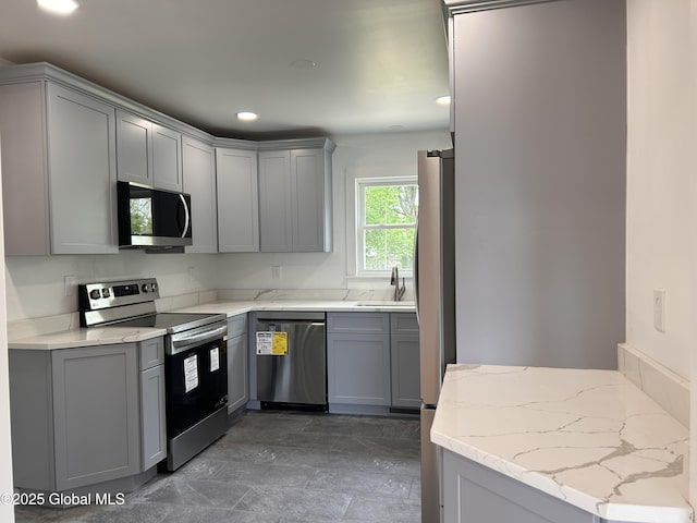 kitchen with stainless steel appliances, gray cabinets, a sink, light stone counters, and recessed lighting