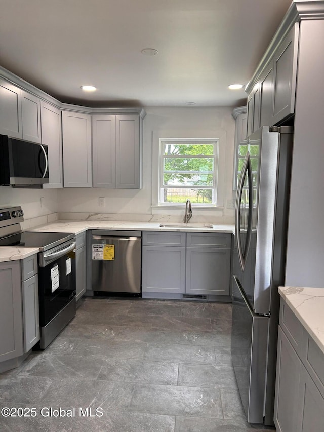 kitchen with stainless steel appliances, a sink, gray cabinetry, light stone countertops, and recessed lighting