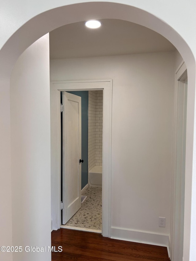 hall with wood finished floors, arched walkways, and baseboards