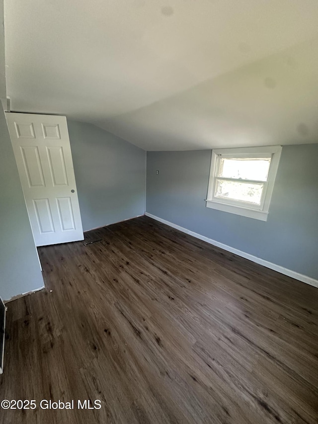 unfurnished room with vaulted ceiling, dark wood-type flooring, and baseboards