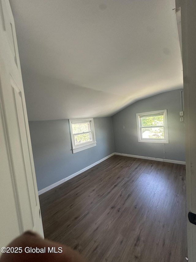 empty room with vaulted ceiling, dark wood-style floors, and baseboards