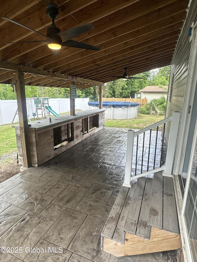 view of patio / terrace with a ceiling fan, a fenced backyard, a covered pool, and a playground