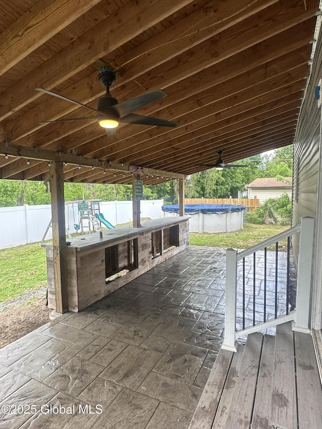 wooden deck with a playground, ceiling fan, a covered pool, and a fenced backyard