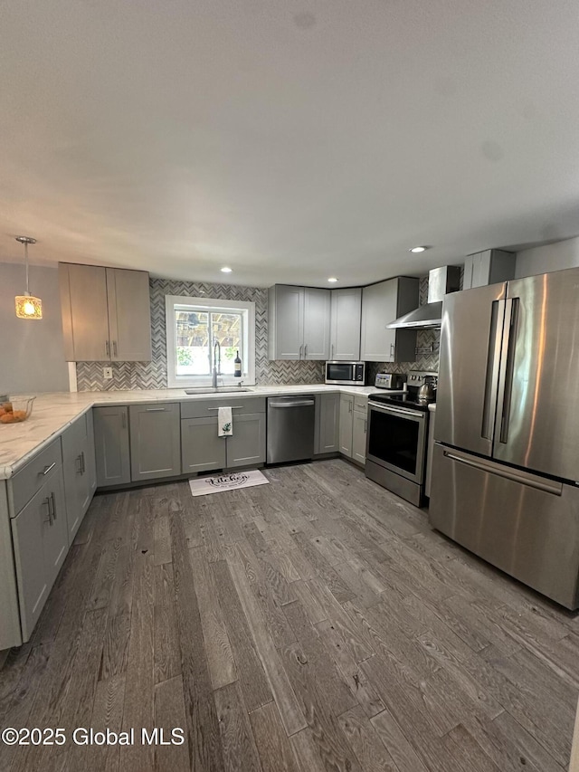 kitchen featuring appliances with stainless steel finishes, wall chimney exhaust hood, dark wood-type flooring, a sink, and tasteful backsplash